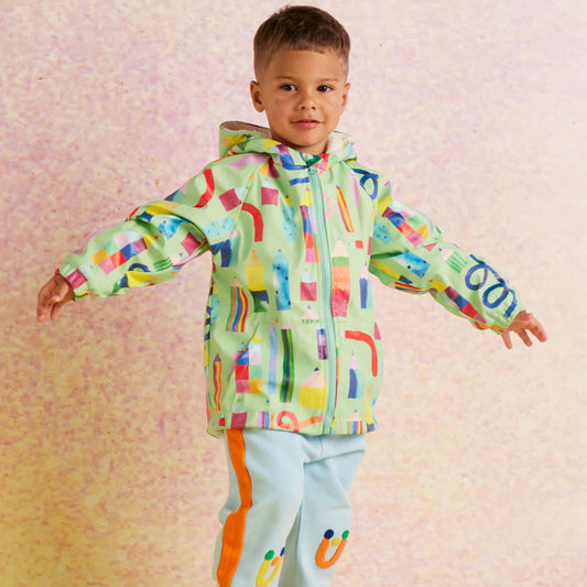 Child wearing a colorful raincoat and light blue pants with rainbow stripes on a pink background