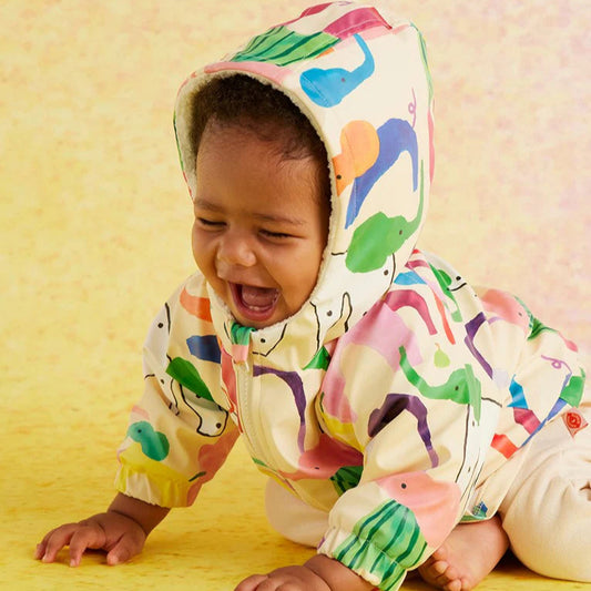 Child wearing a colorful raincoat with dinosaur patterns on a yellow background