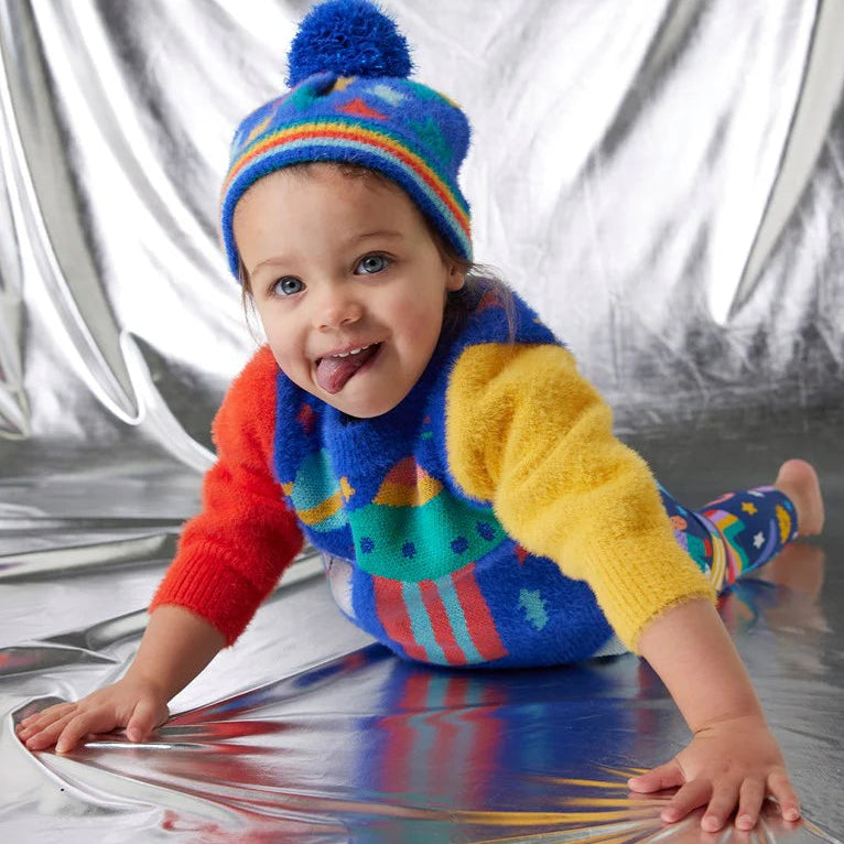 Child wearing a colorful outfit and hat on a reflective surface