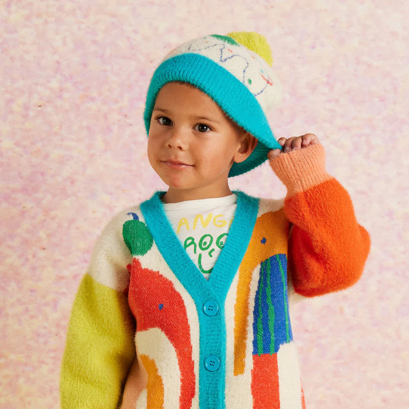 Child wearing a colorful cardigan and hat on a light pink background
